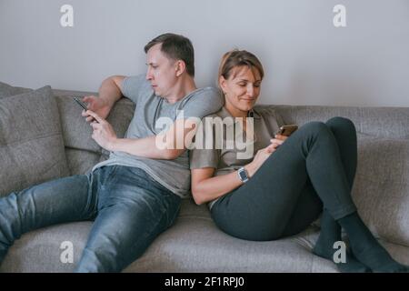 Homme et femme assis sur un canapé et tenant un smartphone entre leurs mains. Banque D'Images