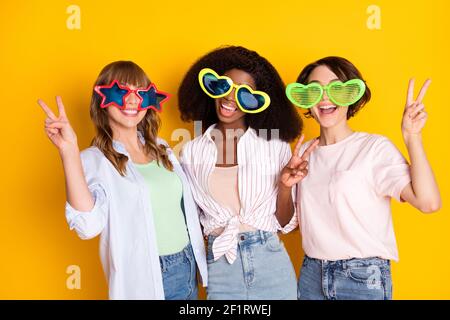 Portrait de jolies filles tendance et gaies qui embrassent le port de V-sign grandes spécifications isolées sur fond jaune vif Banque D'Images