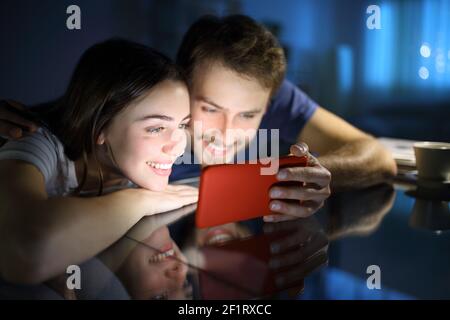 Couple heureux de regarder du contenu multimédia sur un téléphone mobile horizontal dans la nuit à la maison Banque D'Images