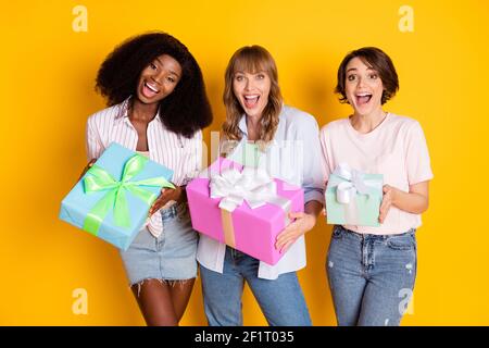 Portrait de trois femmes étonne excitée mains tenir la boîte-cadeau ouverte bouche isolée sur fond jaune Banque D'Images