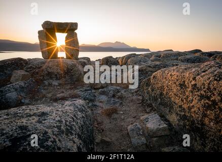 Coucher de soleil à travers Inuksuk dans un paysage arctique accidenté. Sunstar à l'horizon dans le fjord de Qikiqtarjuaq, île Broughton, Nunavut. Le nord. Banque D'Images
