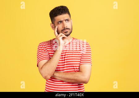 Homme barbu doué dans un t-shirt rayé contemplant la tête penchée sur la main, méditer la question difficile, essayant de faire le bon choix. Studio intérieur s Banque D'Images