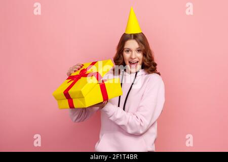 Portrait d'une jeune fille heureuse surprise dans la boîte cadeau à capuche ouvrant et regardant l'appareil photo avec un sourire toroneux, satisfait du présent. Prise de vue en studio Banque D'Images