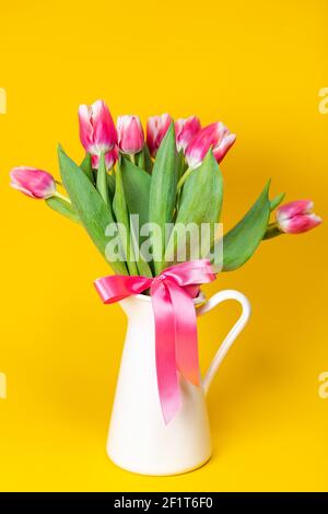 Gros plan d'un pot en porcelaine blanche de rose éclatant tulipes sur fond jaune uni Banque D'Images
