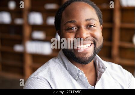 Portrait rapproché d'un jeune homme afro-américain heureux avec un sourire large et chaleureux, un homme barbu de race mixte portant une chemise regarde dans l'appareil photo, photo du profil de l'employé Banque D'Images
