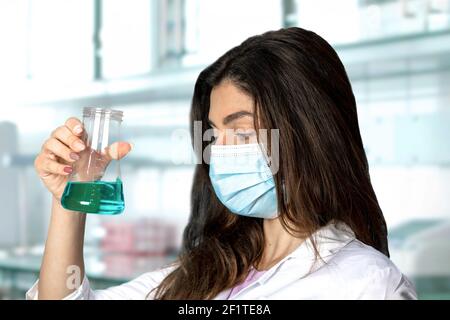 Un chercheur de brunette dans une robe chirurgicale et un masque. En arrière-plan le laboratoire médical flou. Parfait pour la pandémie, la recherche, les vaccins et Banque D'Images