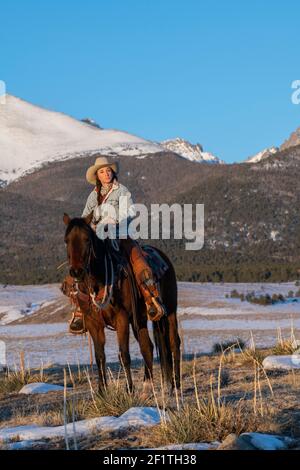 États-Unis, Colorado, Westcliffe, Music Meadows Ranch. Main de ranch femelle dans un ranch typique de l'ouest tenue sur cheval de baie en hiver. Modèle validé. Banque D'Images