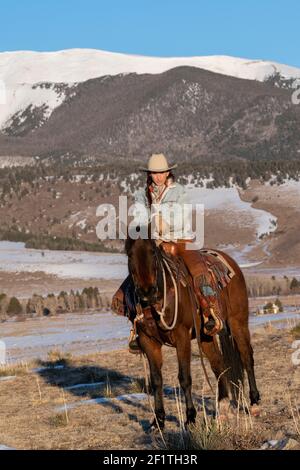 États-Unis, Colorado, Westcliffe, Music Meadows Ranch. Main de ranch femelle dans un ranch typique de l'ouest tenue sur cheval de baie en hiver. Modèle validé. Banque D'Images