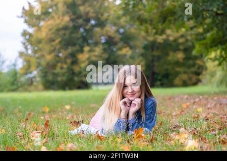 Une jeune fille se trouve sur l'herbe dans une chaude automne dans la soirée avec un pétale dans ses mains. Banque D'Images