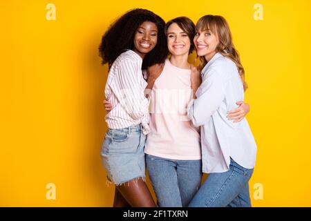 Photo de Nice optimiste trois femmes hug porter chemise blanche jean isolé sur fond jaune vif Banque D'Images