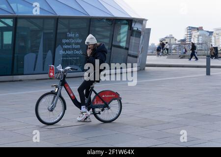 Jeune femme assise sur ses arrêts de vélo Santander loués et vérifie son itinéraire autour de cutty sark pendant sa tournée de Londres greenwich Banque D'Images