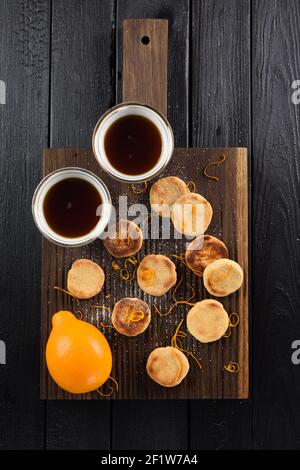 Petits gâteaux faits maison au citron servis sur une planche de chêne avec du citron biologique et thé noir au-dessus de la vue de la tête Banque D'Images