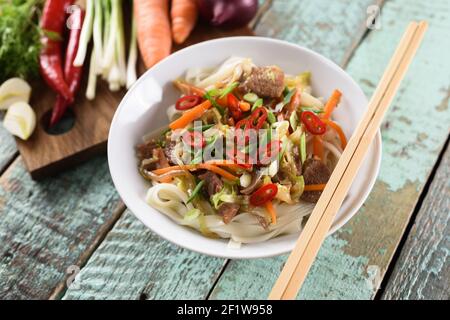 Cuisine asiatique traditionnelle. Nouilles Udon à la viande, aux légumes, au Chili et à l'oignon nouveau dans un bol blanc sur fond de bois rustique bleu pâle. Vue au plafond Banque D'Images