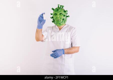 Personne déguisée comme coronavirus avec un masque de latex - virus Covid-19, portant un costume de médecin, prenant un inhalateur d'asthme, sur fond blanc. Coronavi Banque D'Images