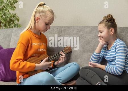 deux adolescentes s'assoient sur le canapé et jouent Ukulele hawaïen Banque D'Images