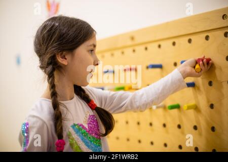 la fille joue avec des panneaux perforés en bois avec des chevilles rondes Banque D'Images