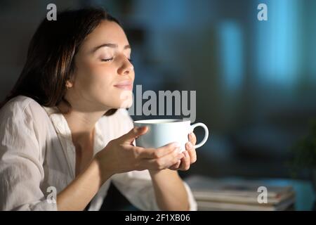 Femme détendue sentant du café décaféiné la nuit à la maison Banque D'Images