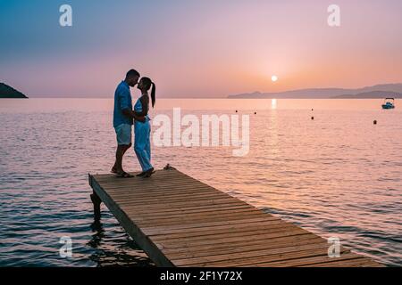 Crète Grèce, jeune couple romantique amoureux est assis et embrassant sur la jetée en bois à la plage au lever du soleil avec le ciel doré. Banque D'Images