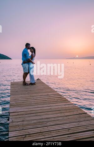 Crète Grèce, jeune couple romantique amoureux est assis et embrassant sur la jetée en bois à la plage au lever du soleil avec le ciel doré. Banque D'Images
