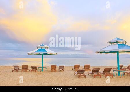 Chaises longues sur la plage. Parasols du soleil avec des sièges sur le lac. La surface de la mer est dégagée sous un ciel bleu. Océan par temps clair. Transats en bois latés. Plage dans une pension ou un hôtel. Vacances. Banque D'Images