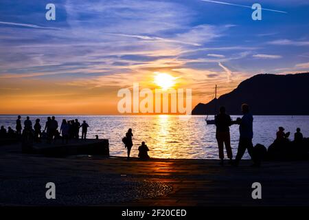 Les touristes sont vus en silhouette le long de la baie et du port de Vernazza, en Italie, le long de la côte des Cinque Terre près du coucher du soleil. Banque D'Images