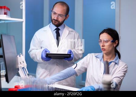 Une équipe professionnelle de chercheurs médicaux travaillant ensemble en laboratoire stérile portant des lunettes de protection et une blouse blanche. Biochimiste médecins analysant une expérience médicale pour découvrir un vaccin Banque D'Images