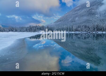 Allemagne, Bavière, Berchtesgaden, Alpes Berchtesgadener, partiellement couvert de neige et gelé Lac Hintersee avec reflet du ciel, des collines et des nuages dans la section non gelée. Banque D'Images