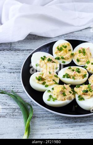 œufs farcis avec bâtonnets de crabe, mayonnaise, fromage et oignon vert sur une assiette noire. Arrière-plan blanc Banque D'Images