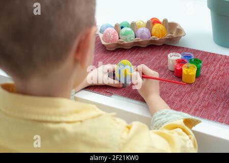 Petit garçon caucasien créatif peignant des œufs de Pâques. Enfant d'âge préscolaire décorer et peindre les œufs de pâques dans des couleurs différentes. Préparation pour l'EAS des fêtes Banque D'Images