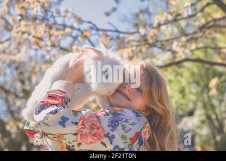Adorable fille adorable avec de longs cheveux blonds embrassant les Pâques blanches animal de lapin dans la nature magique et colorée du printemps sous les arbres Banque D'Images