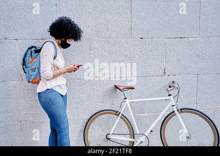 Femme afro-américaine avec un smartphone dans la main. Femme avec masque de protection. Vélo dans la ville. Photo de haute qualité Banque D'Images