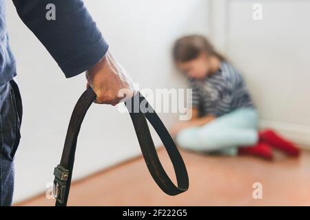 La fille est assise dans le coin se cachant de son beau-père abusif. Le concept de l'éducation des enfants par la violence domestique. Punition pour un crim Banque D'Images