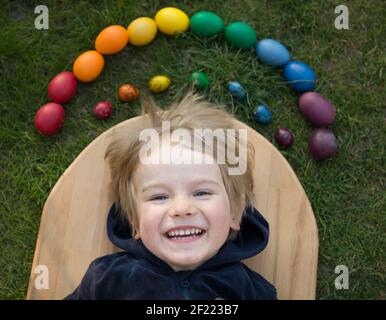 Un jeune garçon heureux se trouve près du poulet et des œufs de caille peints aux couleurs vives de l'arc-en-ciel, vacances de printemps ensoleillées. Traditions familiales. Joyeux jour de lumière d'EA Banque D'Images