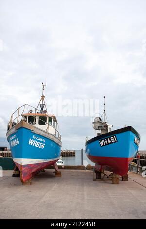 Bateaux de pêche bleus et rouges sur le dur à Bridport Harbour, West Bay, Dorset Banque D'Images