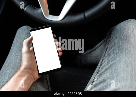 Vue intérieure d'une nouvelle voiture moderne. Jeune conducteur utilisant un téléphone intelligent dans la voiture pendant la conduite ou le stationnement. Maquette d'un téléphone mobile wi Banque D'Images