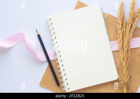 Carnet blanc vierge avec ligne ou bloc-notes et crayon ou stylo noir près de la fleur séchée sur fond blanc de bureau avec espace de copie dans le plan de travail de la vue de dessus. Bus Banque D'Images