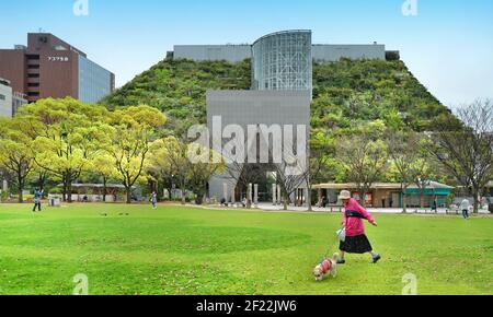 Femme marchant avec son chien devant le hall international de la préfecture d'ACROS Fukuoka à Tenjin Central Park, Fukuoka, Japon, architecte: Emilio Ambasz Banque D'Images