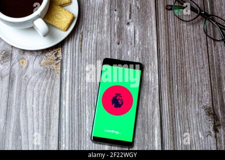 Un téléphone portable ou un téléphone portable sur une table en bois Avec l'application Premier League ouverte à côté d'un café et lunettes Banque D'Images