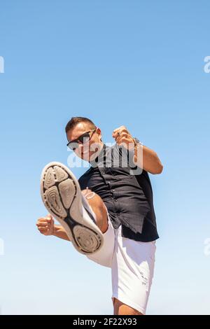 Un jeune homme dans une chemise noire donne un coup de pied vers la caméra. Banque D'Images