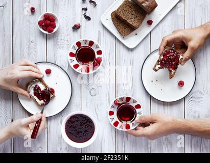 Homme et femme buvant du thé et mangeant des toasts à la framboise gelée au petit déjeuner sur une table en bois blanc Banque D'Images