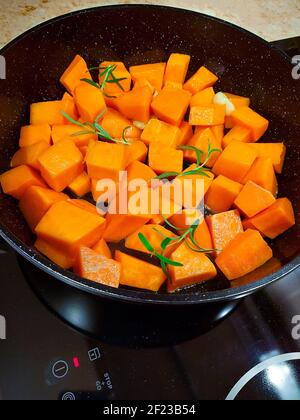 Morceaux de citrouille orange vif avec branches de romarin vert sur une poêle noire Banque D'Images