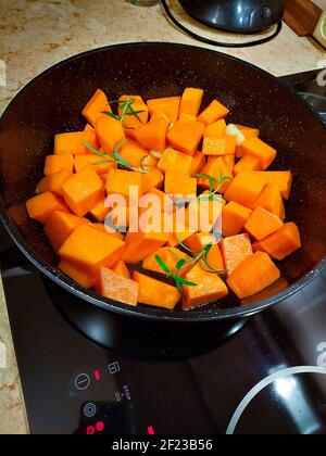 Morceaux de citrouille orange vif avec branches de romarin vert sur une poêle noire Banque D'Images