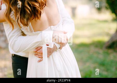 La mariée et le marié embrassent dans le parc, le marié met ses mains sur le dos de la mariée Banque D'Images
