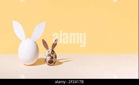 Un œuf de poulet et une caille avec des oreilles de lapin de pâques sur fond beige et jaune, concept moderne isométrique de pâques, espace de copie, gros plan. Banque D'Images