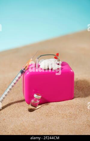 une seringue, un flacon, un avion et une valise rose sur le sable, sur fond bleu, représentant le tourisme médical Banque D'Images