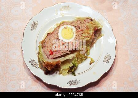 Morceau de pain de viande en feuilles de chou de Savoie dans une assiette de service vintage. Un demi-œuf au centre de la coupe, beaucoup de viande hachée épicée, semble deli Banque D'Images