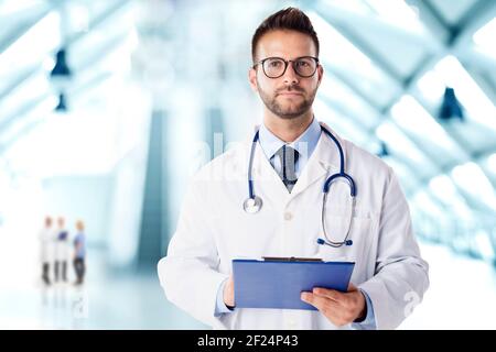 Portrait d'un médecin souriant avec stéthoscope autour de son cou, debout dans le foyer de l'hôpital tout en tenant le presse-papiers dans sa main. Copier l'espace. Banque D'Images