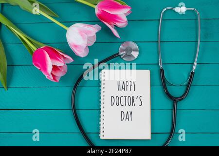 Tulipes roses et stéthoscope avec bloc-notes en spirale avec texte « Happy Doctors Day ». plan d'examen en plan, Banque D'Images