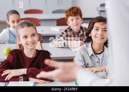 des écoliers heureux à l'écoute de l'enseignant en classe sur un premier plan flou Banque D'Images