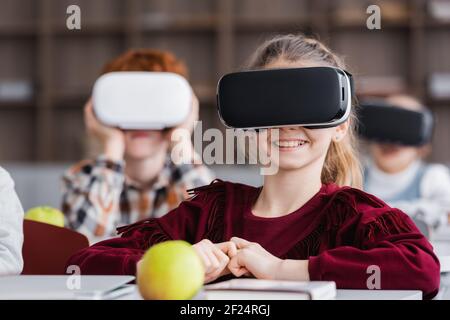 une fille enjouée dans un micro-casque vr entend ses camarades de classe sur flou arrière-plan Banque D'Images